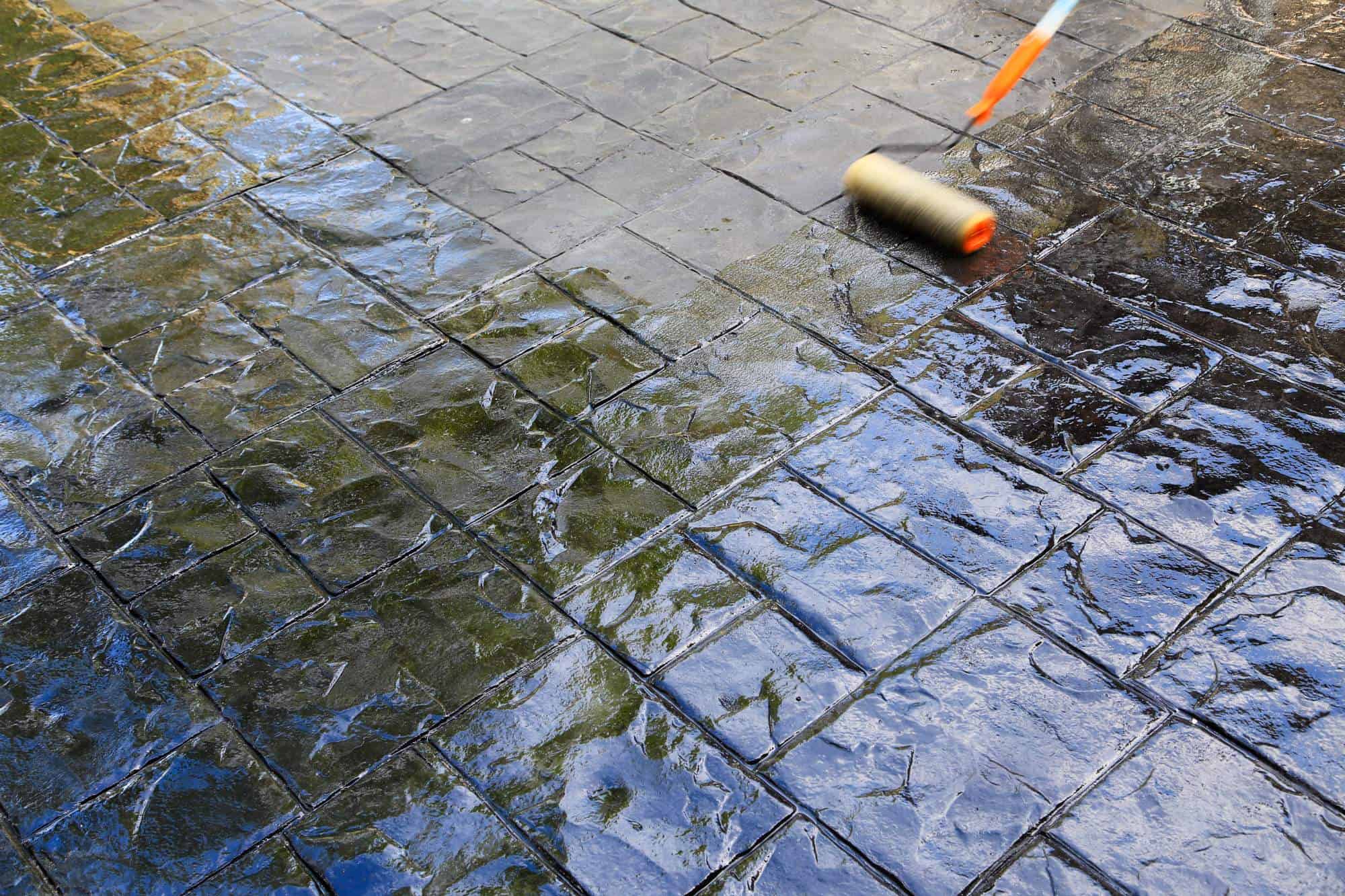 A paint roller is being used to apply seal coating Maricopa County to a textured, stamped concrete surface, enhancing its appearance and protecting it.