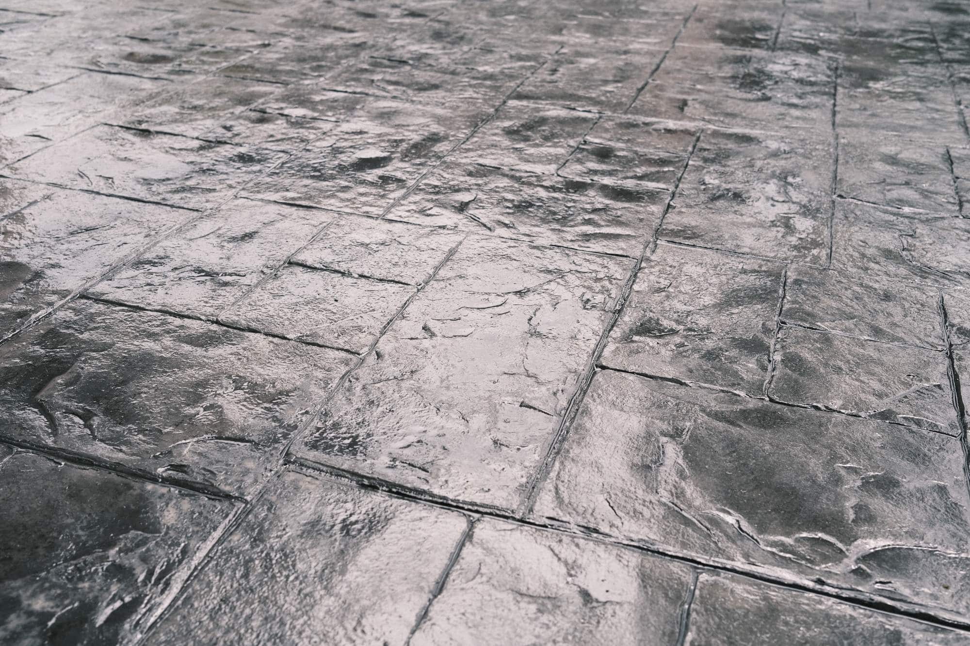 Close-up view of a wet, stamped concrete surface designed to resemble stone tiles, featuring a shiny texture and visible reflections—ideal for seal coating Maricopa County or garage floor coating in AZ.