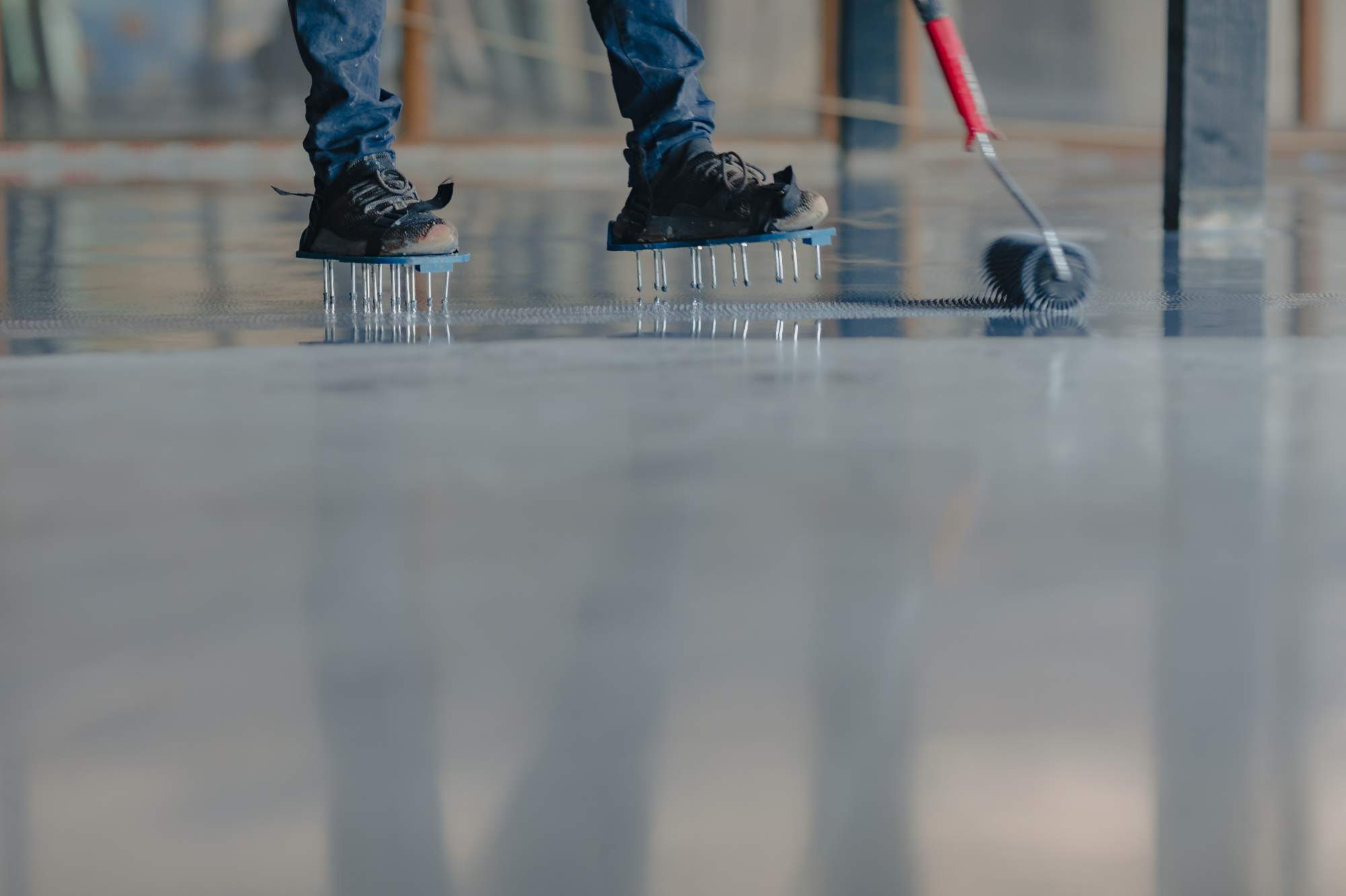 A person wearing spiked shoes uses a roller to apply and spread epoxy resin on a floor, showcasing the process of garage floor coating in Maricopa County, AZ, likely for a construction or renovation project.