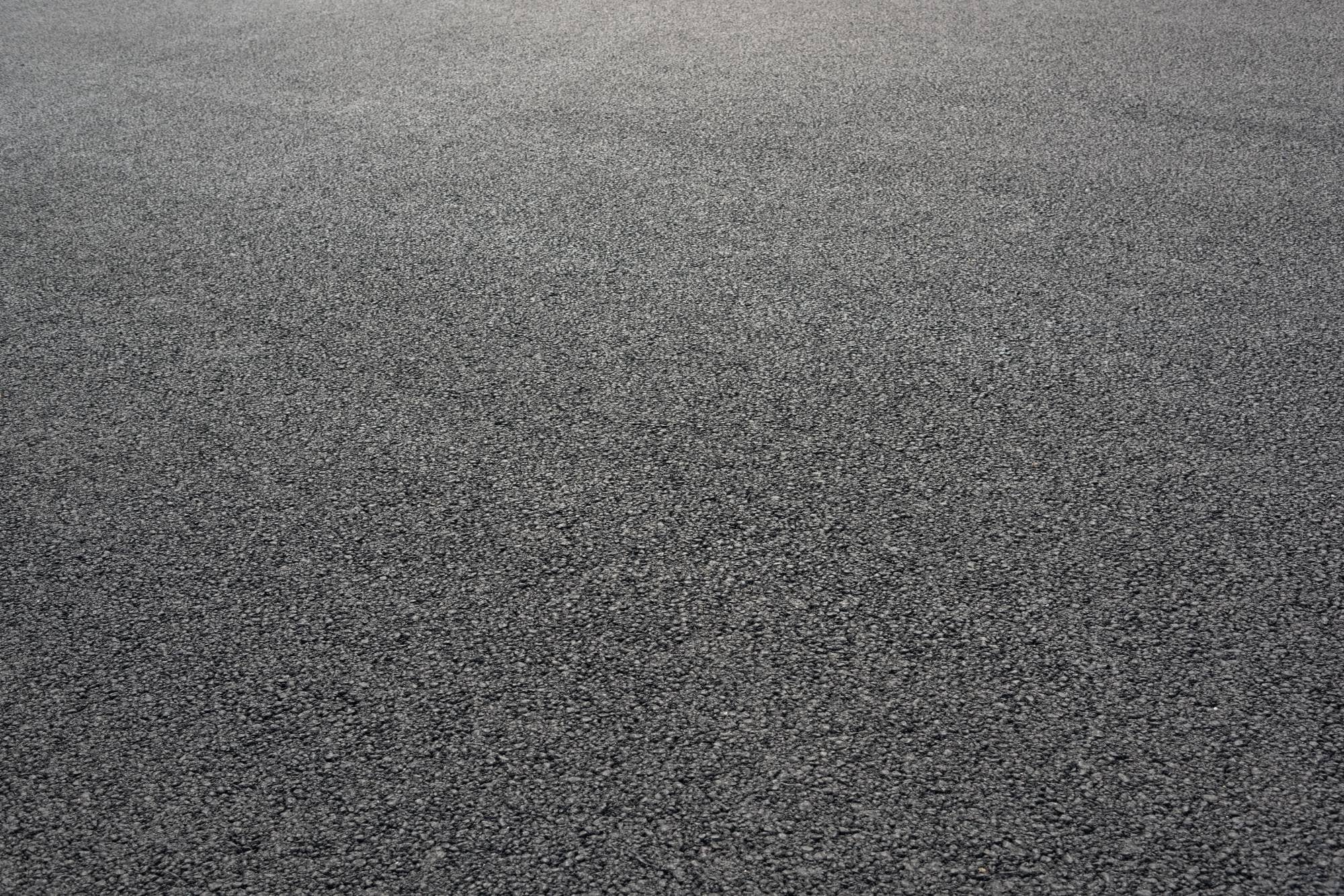 A close-up view of a flat, smooth, dark gray asphalt surface, freshly finished with seal coating Maricopa County, AZ—subtle texture hints at quality craftsmanship with no visible markings or objects.
